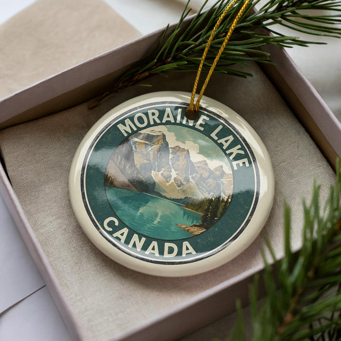 A circular ornament with a mountain landscape and a lake, surrounded by greenery, is displayed in a box.