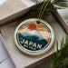 A circular ornament with a mountain and sun design, featuring the text "JAPAN Mt. fuji".