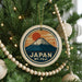 A Christmas tree decorated with ornaments, including a circular ornament with a mountain and sun design, and a string of wooden beads.