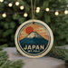 A circular ornament with a mountain and sun design, featuring the text "JAPAN MT. FUJI" on it, is hanging from a string.