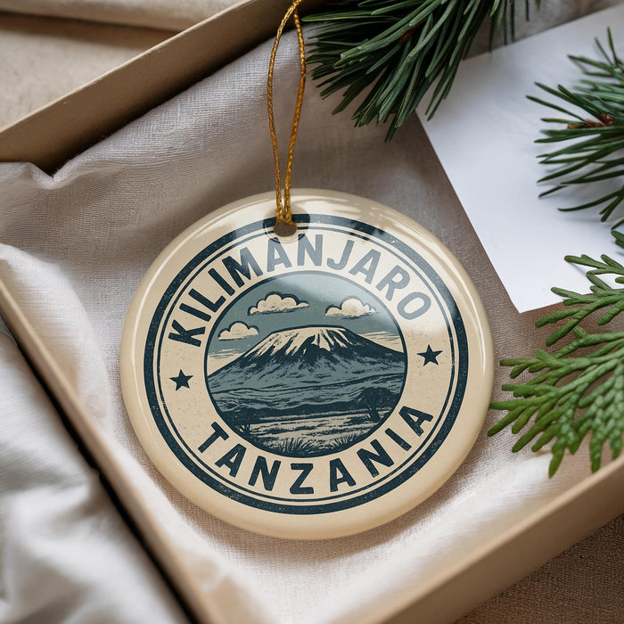 A decorative ornament with the text "KILIMANJARO TANZANIA" printed on it, surrounded by a circular design featuring a mountain and clouds.