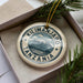 A circular ornament with the text "KILIMANJARO TANZANIA" printed on it, surrounded by a border and a mountain illustration.