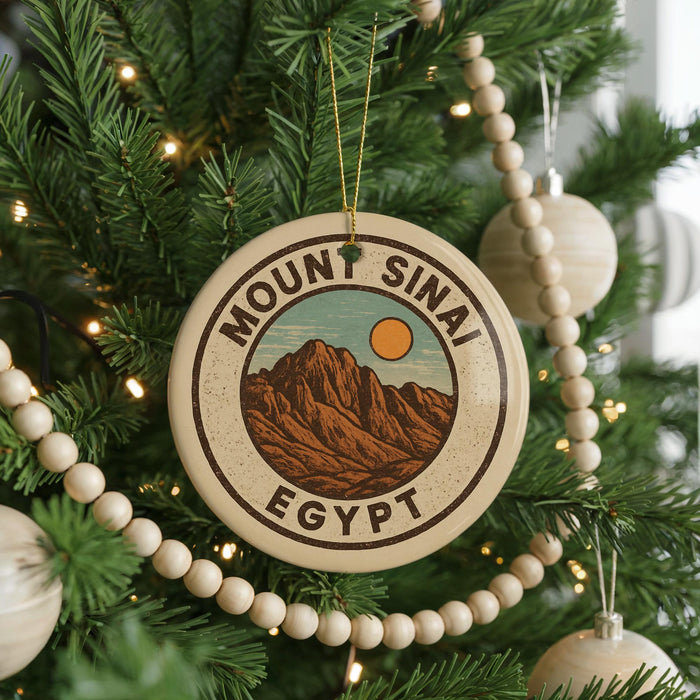A Christmas tree decorated with ornaments, including a circular ornament with a mountain and sun design, surrounded by lights and greenery.