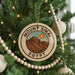 A Christmas tree decorated with ornaments, including a circular ornament with a mountain and sun design, surrounded by lights and greenery.