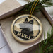 A circular ornament with a black and white image of a dog's head and the word "MUDI" written below it, hanging from a string.