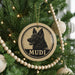 A Christmas tree decorated with ornaments, including a circular ornament with a dog's head and the word "MUDI" written on it.