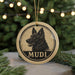 A circular ornament with a black and white illustration of a dog's head and the word "MUDI" written below it, hanging from a string.