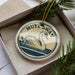 A decorative ornament in a box, featuring a swan image and the text "MUTES SWAN".