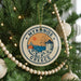A circular ornament on a Christmas tree, featuring a design of a windmill and the text "MYKONOS GREECE".