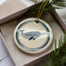 A ceramic ornament in a box, featuring a blue and white design of a whale or dolphin.