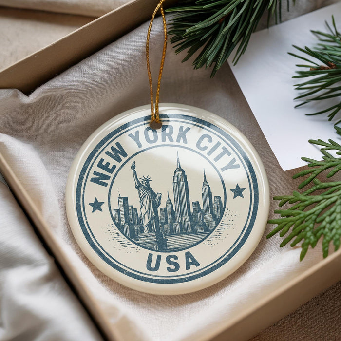 A decorative ornament with the text "NEW YORK CITY USA" and an illustration of the Statue of Liberty, placed in a box with pine branches.