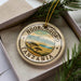 A circular ornament with the text "NGORONGORO TANZANIA" printed on it, surrounded by a border and a landscape illustration.