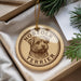 A round ornament with a dog image and the text "NORFOLK TERRIER" printed on it, placed in a box with pine branches.