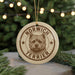 A round ornament featuring a terrier dog's head, with the text "NORWICH TERRIER" printed on it, hanging from a string.