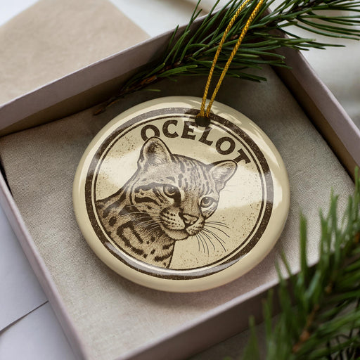 A circular ornament with a cat image and the word "OCELOT" written on it, placed inside a box with pine branches.
