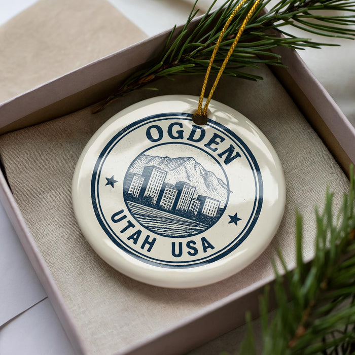 A decorative ornament in a box, featuring a circular design with a mountain and cityscape, and the text "OGDEN UTAH USA".