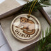A round ornament with a brown and white design depicting a brown animal, possibly a rodent or small mammal, sitting on a branch. The word "OLINGO" is written below the image.