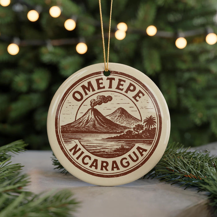 A circular ornament with the text "OMETOPE" and "NICARAGUA" printed on it, hanging from a string. The ornament is surrounded by pine branches and is placed on a surface with a blurred background of greenery and lights.