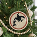 A Christmas tree decorated with ornaments, including a circular ornament featuring a black and white orca whale silhouette.