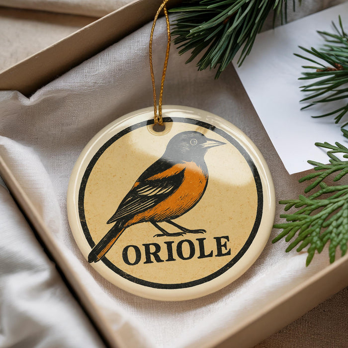 A circular ornament with an illustration of an oriole bird and the word "ORIOLE" printed on it, hanging from a string.