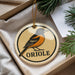 A circular ornament with an illustration of an oriole bird and the word "ORIOLE" printed on it, hanging from a string.