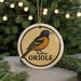 A ceramic ornament featuring an illustration of an oriole bird, with the word "ORIORE" written below it.