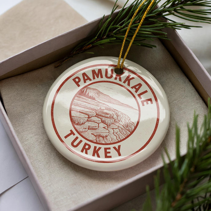A circular ornament with the text "PAMUKKALE TURKEY" printed on it, placed inside a box with pine branches.