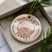 A circular ornament with the text "PAMUKKALE TURKEY" printed on it, placed inside a box with pine branches.