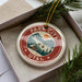 A circular ornament with the text "PARK CITY UTAH" and an illustration of a mountain range, pine trees, and a ski lift.