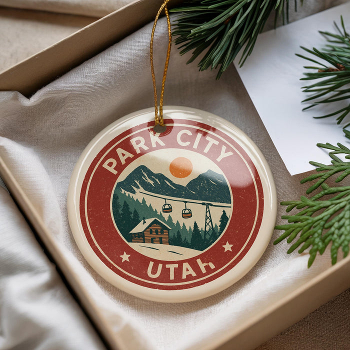 A circular ornament with a red border and a graphic design depicting a mountain landscape with ski lifts, surrounded by pine branches.