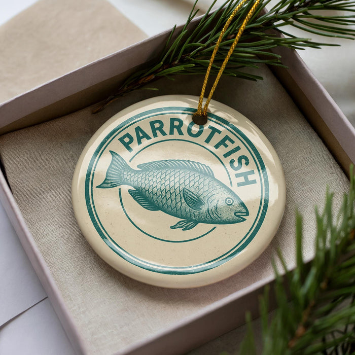 A circular ornament with the word "PARROTFISH" written on it, featuring a fish illustration, is displayed in a box with pine branches.
