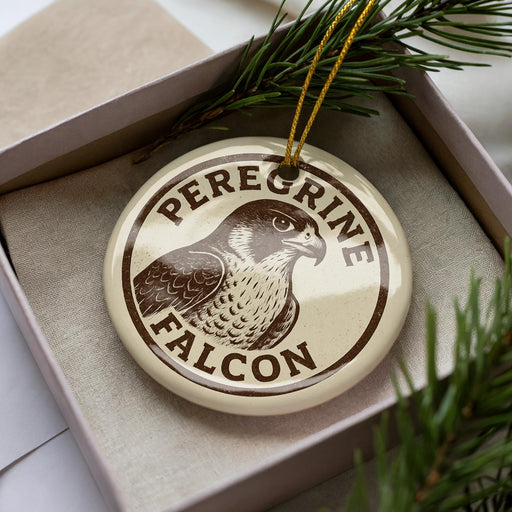 A circular ornament with the text "Peregrine Falcon" printed on it, surrounded by pine branches.