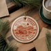 A circular ornament with the text "PETRIFIED FOREST NATIONAL PARK USA" printed on it, surrounded by pine branches and a cup of coffee on a wooden surface.