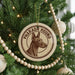 A round ornament with a picture of a dog, specifically a hound, is hanging on a Christmas tree.