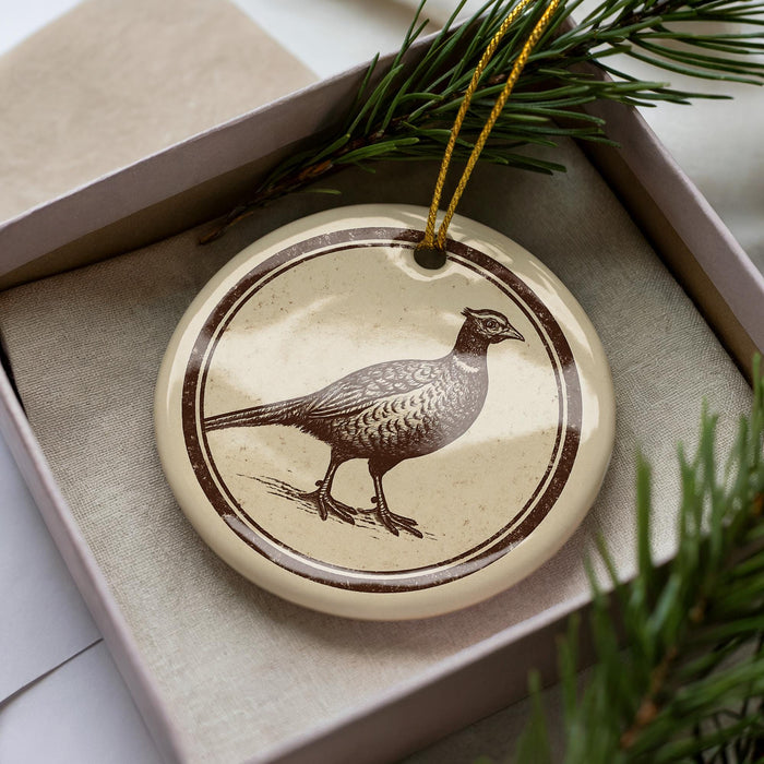 A ceramic ornament in the shape of a bird, possibly a pheasant, is displayed in a box with pine branches.
