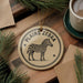 a decorative ornament with a zebra illustration, placed on a wooden surface alongside a cup of coffee and some pine branches.