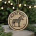 A round ornament featuring a zebra illustration, with the text "PLANS ZEBRA" printed on it, is displayed in front of a blurred Christmas tree.