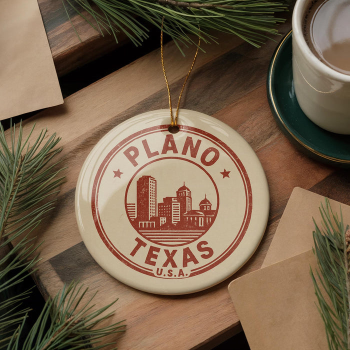 A circular ornament with the text "PLANO TEXAS U.S.A." printed on it, surrounded by pine branches and a cup of coffee on a wooden surface.
