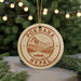 A circular ornament with the text "POKHARA NEPA" and an illustration of a mountain and a boat on a lake, hanging from a string.
