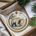 A polar bear ornament is displayed in a box, surrounded by pine branches.