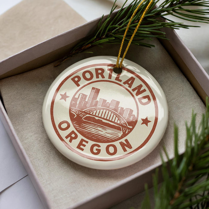A decorative ornament in the shape of a city skyline, with the text "PORTLAND OREGON" prominently displayed, is placed in a box surrounded by pine branches.