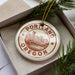 A decorative ornament in the shape of a city skyline, with the text "PORTLAND OREGON" prominently displayed, is placed in a box surrounded by pine branches.