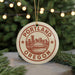 A round ornament with the text "PORTLAND OREGON" and an illustration of a city skyline, hanging from a string.