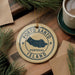 A circular ornament with the text "PORTO SANTO PORTUGAL ISLAND" printed on it, surrounded by pine branches and a cup of coffee on a wooden surface.
