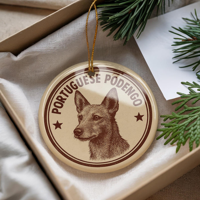 A circular ornament with a brown and tan design featuring a dog's head and the text "PORTUGUESE PODENGO" is displayed in a box with pine branches.
