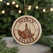 A circular ornament with the text "POZNAN POLAND" and an illustration of a building, hanging from a string against a blurred background of Christmas lights.