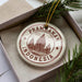 A circular ornament with the text "Prambanan Indonesia" printed on it, surrounded by a decorative border and a pine branch.