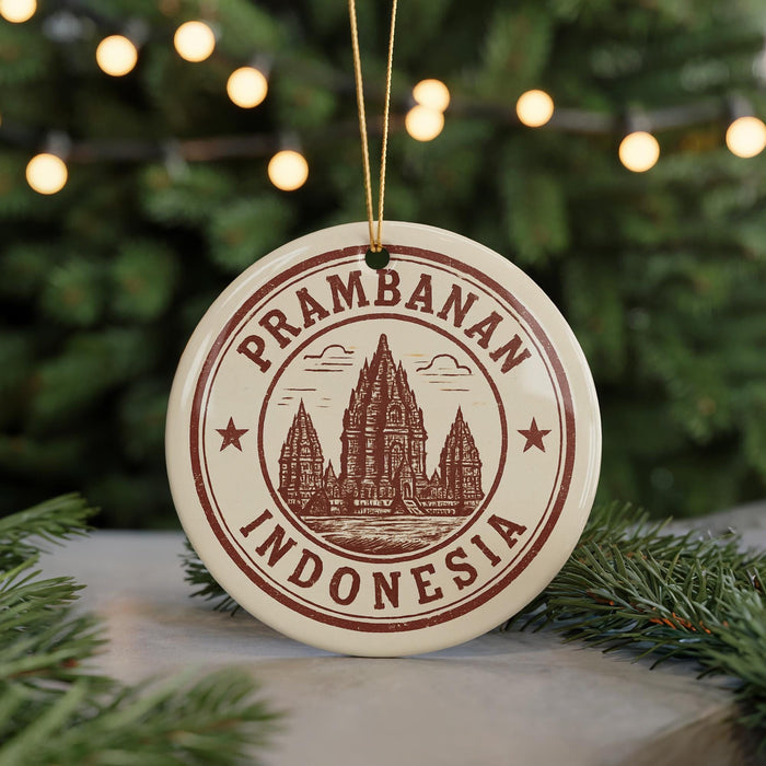 A circular ornament with the text "Prambanan Indonesia" and an illustration of a temple, hanging from a string against a background of Christmas lights and greenery.