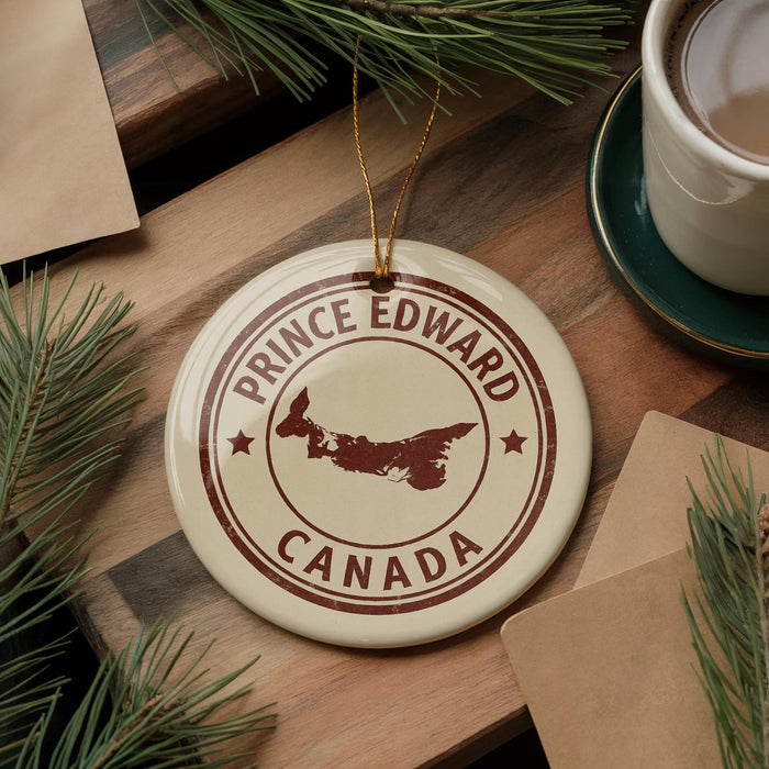 A circular ornament with the text "PRINCE EDWARD CANADA" and a map of Prince Edward Island, a region in Canada, is displayed on a wooden surface alongside a cup of coffee and some pine branches.
