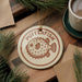 A circular ornament with the word "PUFFERFISH" printed on it, surrounded by pine branches and a cup of coffee on a wooden surface.